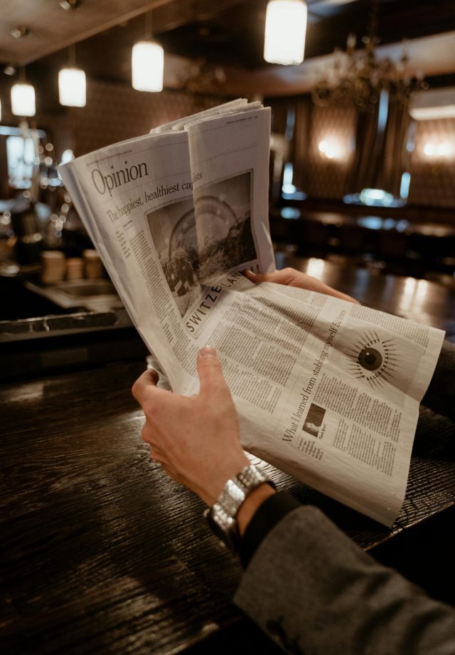 Close-up of hands holding a newspaper in a vintage bar. Warm lighting creates a nostalgic ambiance.